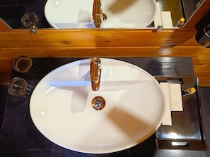 A white oval sink with a single faucet, a mirror above it, and a wooden countertop. - Coco Teros Resort (Mandrem)