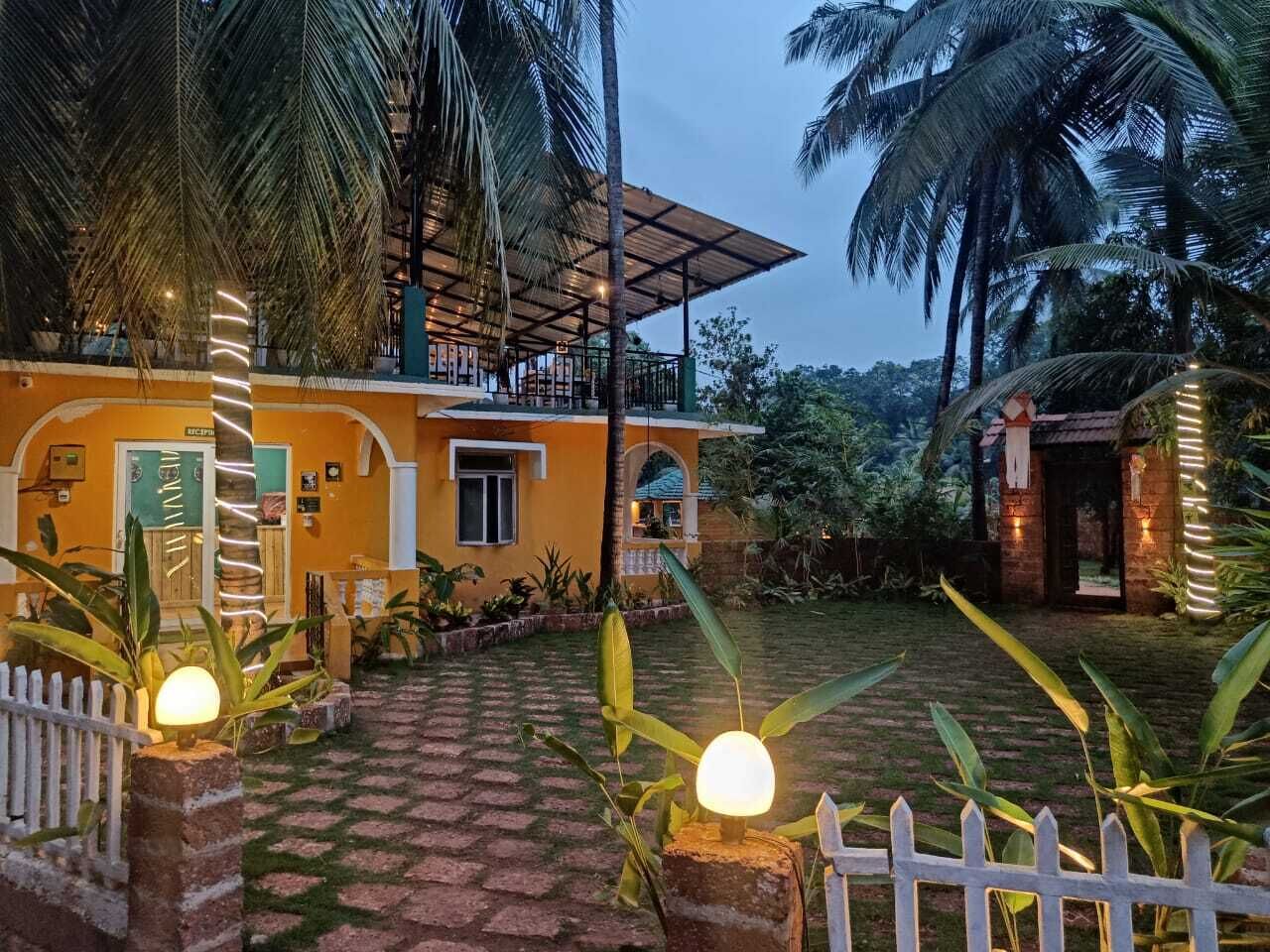 A two-story building with a balcony, surrounded by palm trees and a white picket fence.