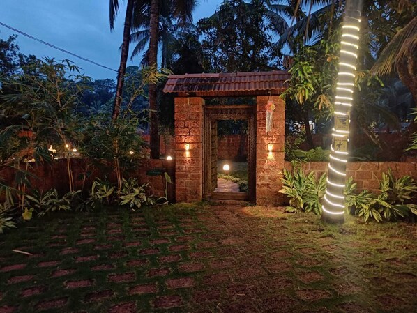 A brick archway leading to a covered entrance, surrounded by lush greenery and a well-lit pathway. - Coco Teros Resort (Mandrem)