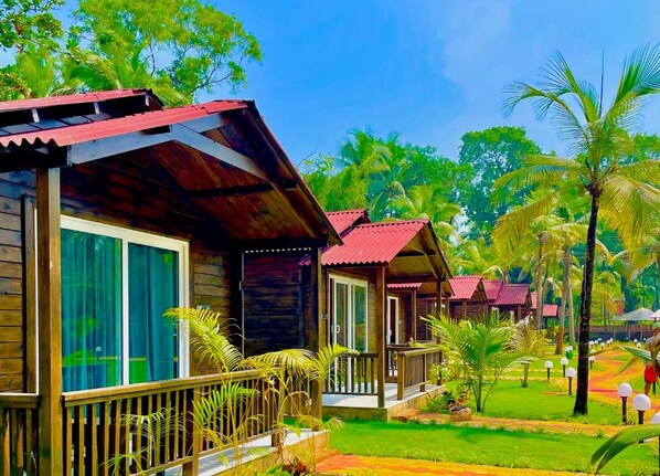 A row of wooden cabins with red roofs, surrounded by lush greenery and palm trees. - Coco Teros Resort (Mandrem)
