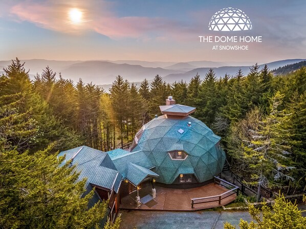 A geodesic dome house surrounded by forest, with a view of distant mountains.