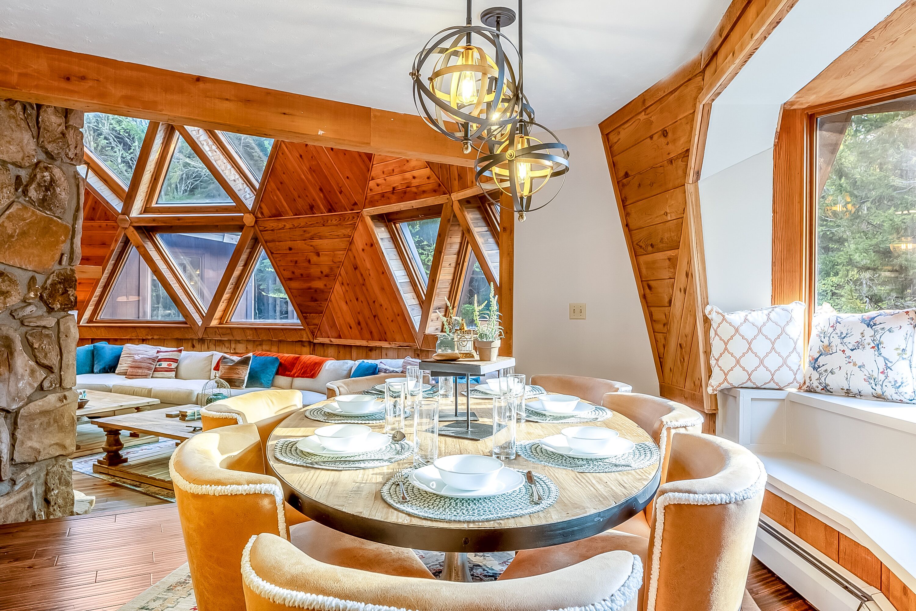 Une pièce chaleureuse avec un plafond en bois, un mur en pierre et une table ronde préparée pour un repas à six personnes.