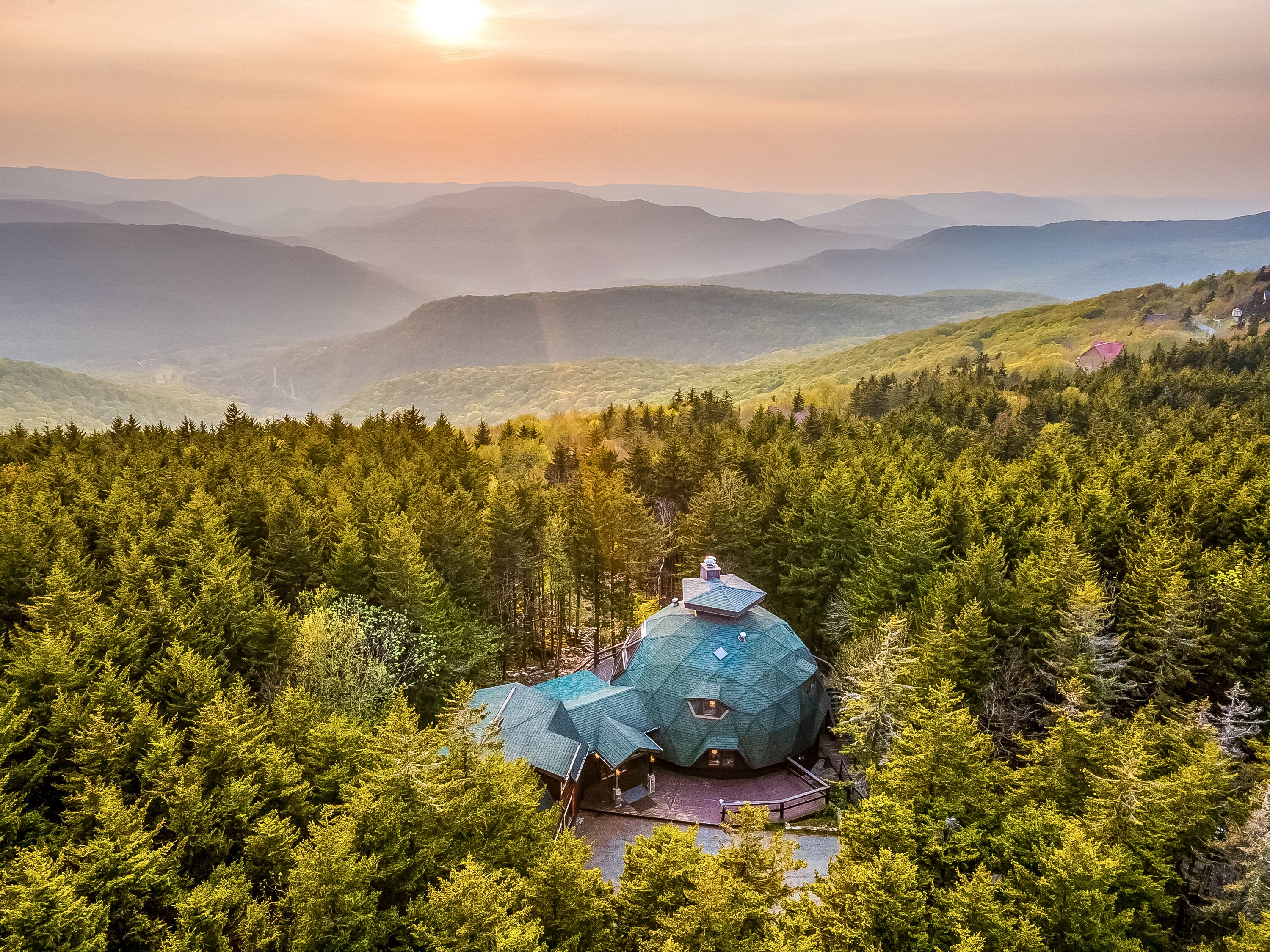 A geodesic dome house surrounded by dense forest, with a view of distant mountains.