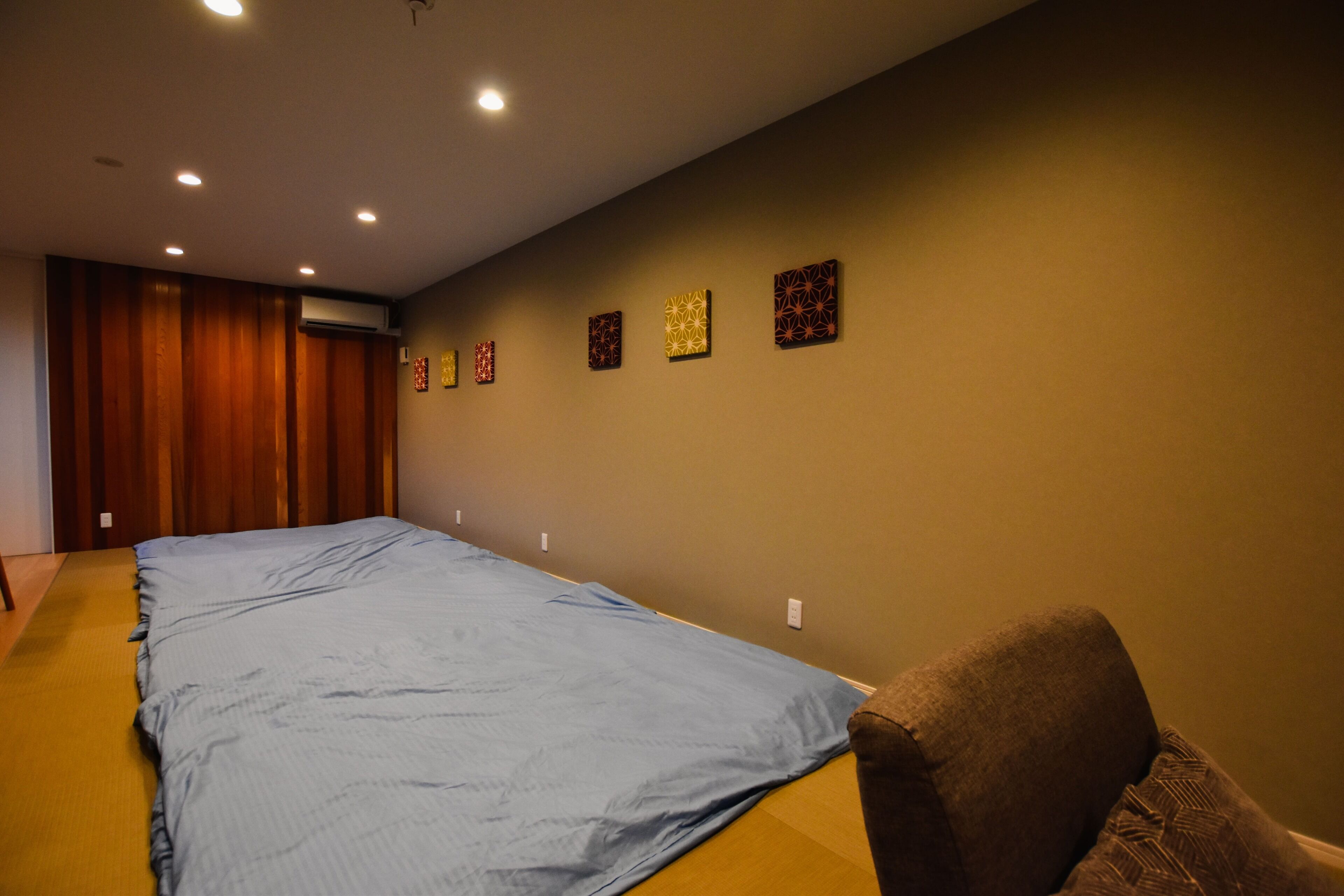 A room with a large bed, a wooden wardrobe, and a wall with framed artwork.