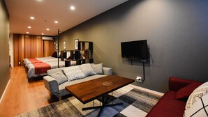 Une chambre d’hôtel moderne avec un canapé, une table basse en bois, un téléviseur fixé au mur et un lit recouvert d’une couverture rouge.