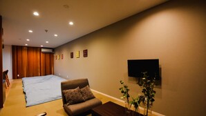 Une pièce comprenant un canapé, une table basse, un téléviseur fixé au mur et un grand lit recouvert d’une couverture bleue.
