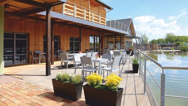 A wooden deck with outdoor seating, overlooking a body of water. - An der Metow-Ferienpark.Hotel (Plau am See)
