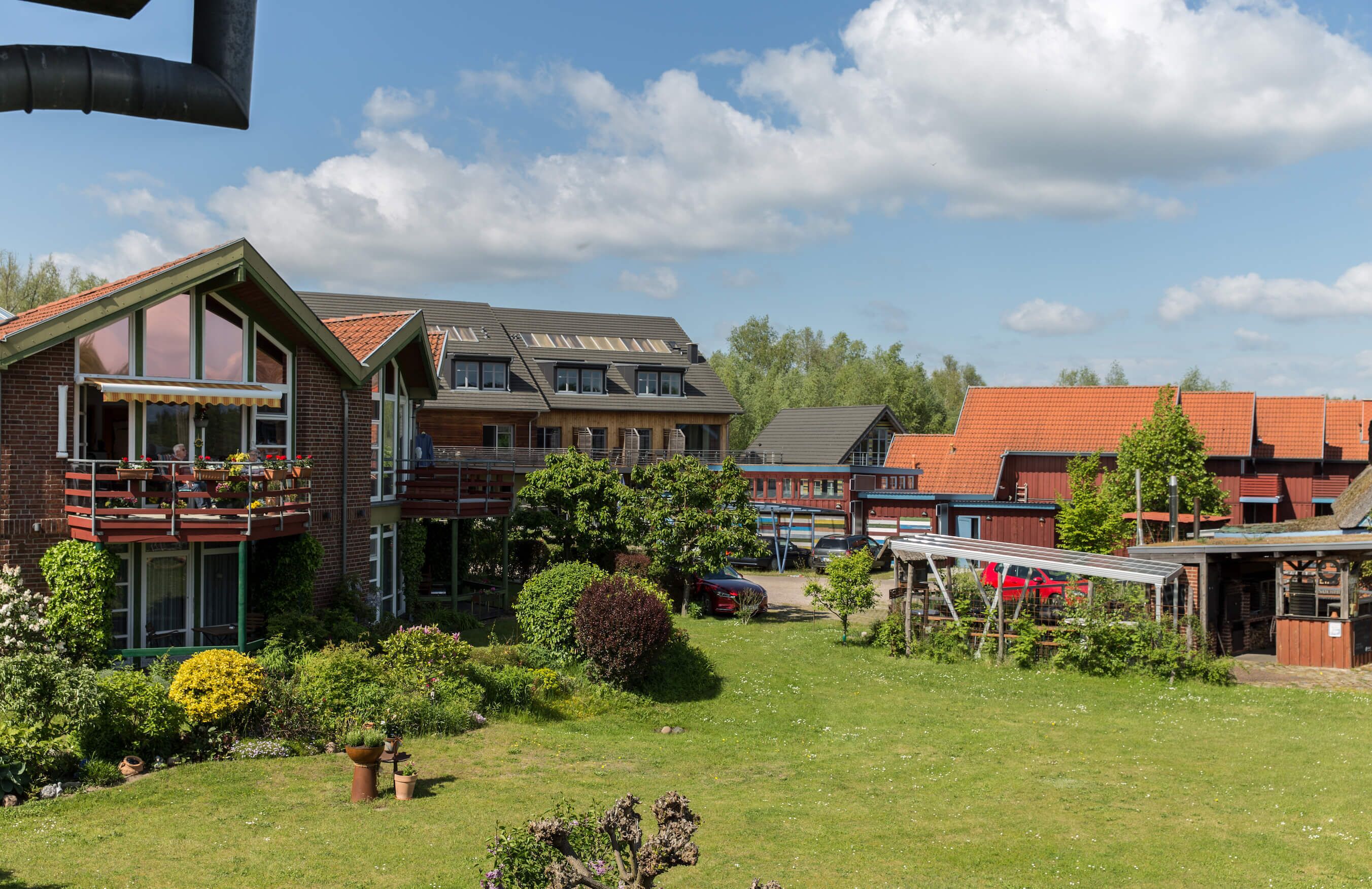 Ett bostadsområde med flera hus, en gräsyta och en röd bil som står parkerad på uppfarten.