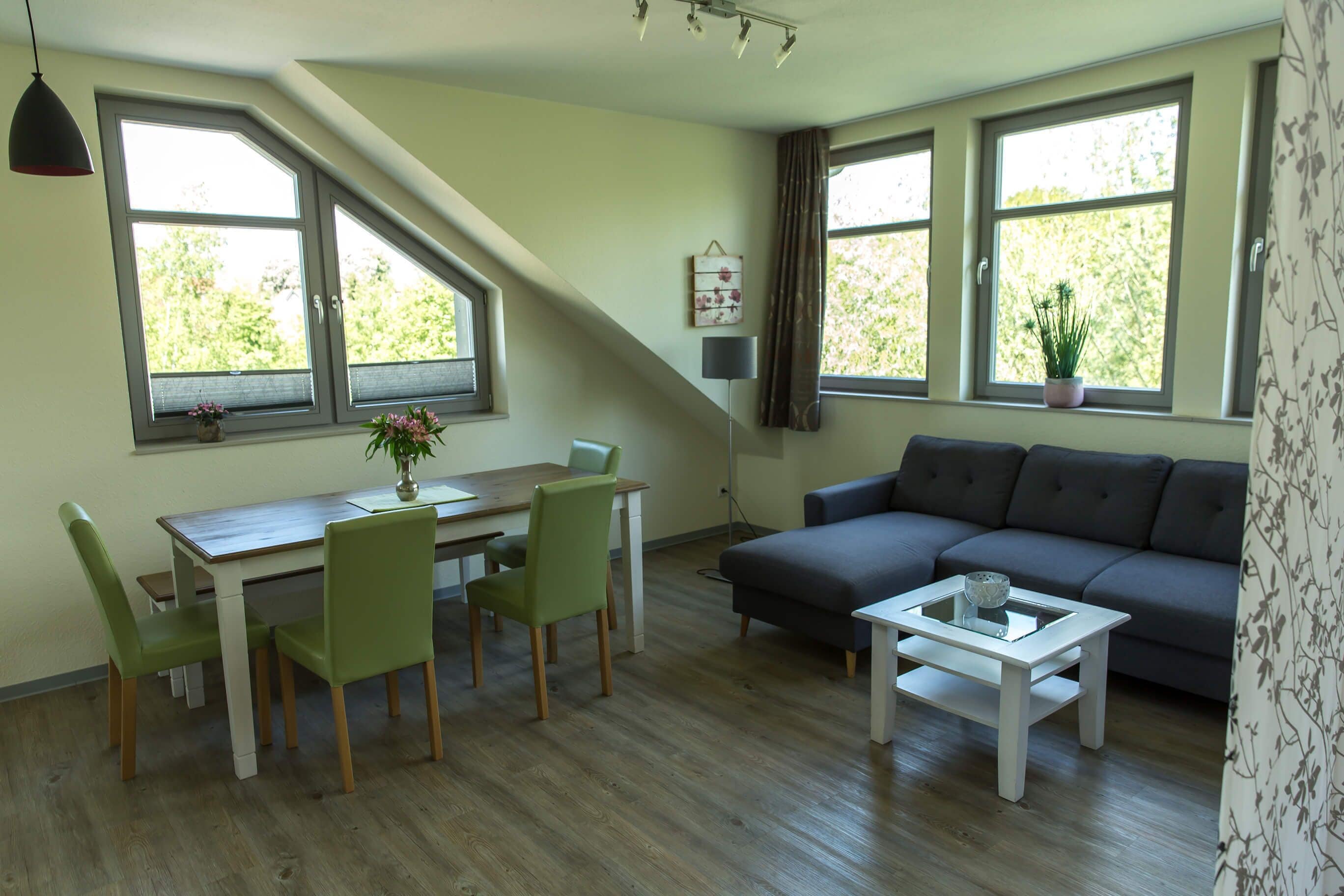 Ein modernes Wohnzimmer mit Essbereich, großen Fenstern und einem grauen Sofa.