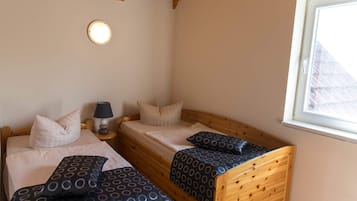 Ein Schlafzimmer mit zwei Holzbettgestellen übereinander, einem Nachttisch mit Lampe und einem Fenster mit Blick auf ein Gebäude.