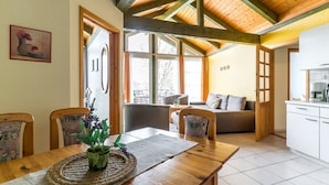 A dining area with a wooden table, chairs, and a plant centerpiece. There is a kitchen visible in the background with white cabinets and a stove. - An der Metow-Ferienpark.Hotel (Plau am See)