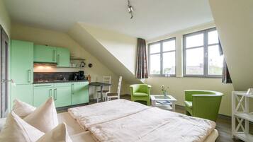 A room with a bed, a kitchenette, a dining area, and a window with curtains.