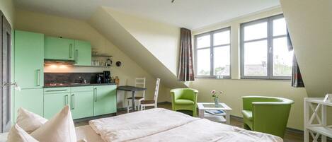 A room with a bed, a kitchenette, a dining area, and a window with curtains.