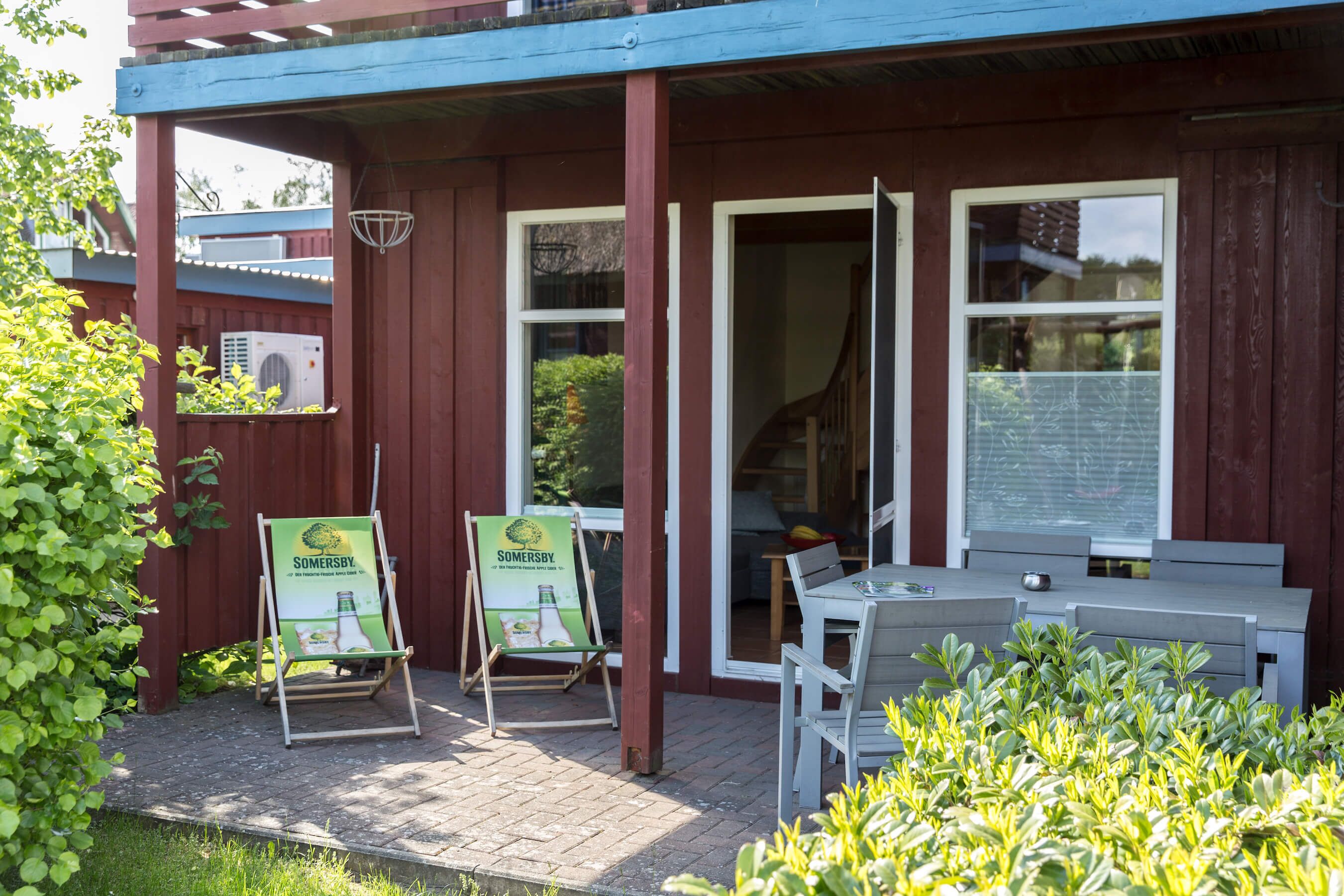 A wooden building with a covered patio area, two green lawn chairs, a table, and a bench.