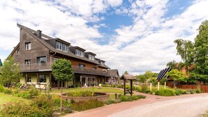 A two-story house with a sloped roof, a front porch, and a garden with a pond. - An der Metow-Ferienpark.Hotel (Plau am See)