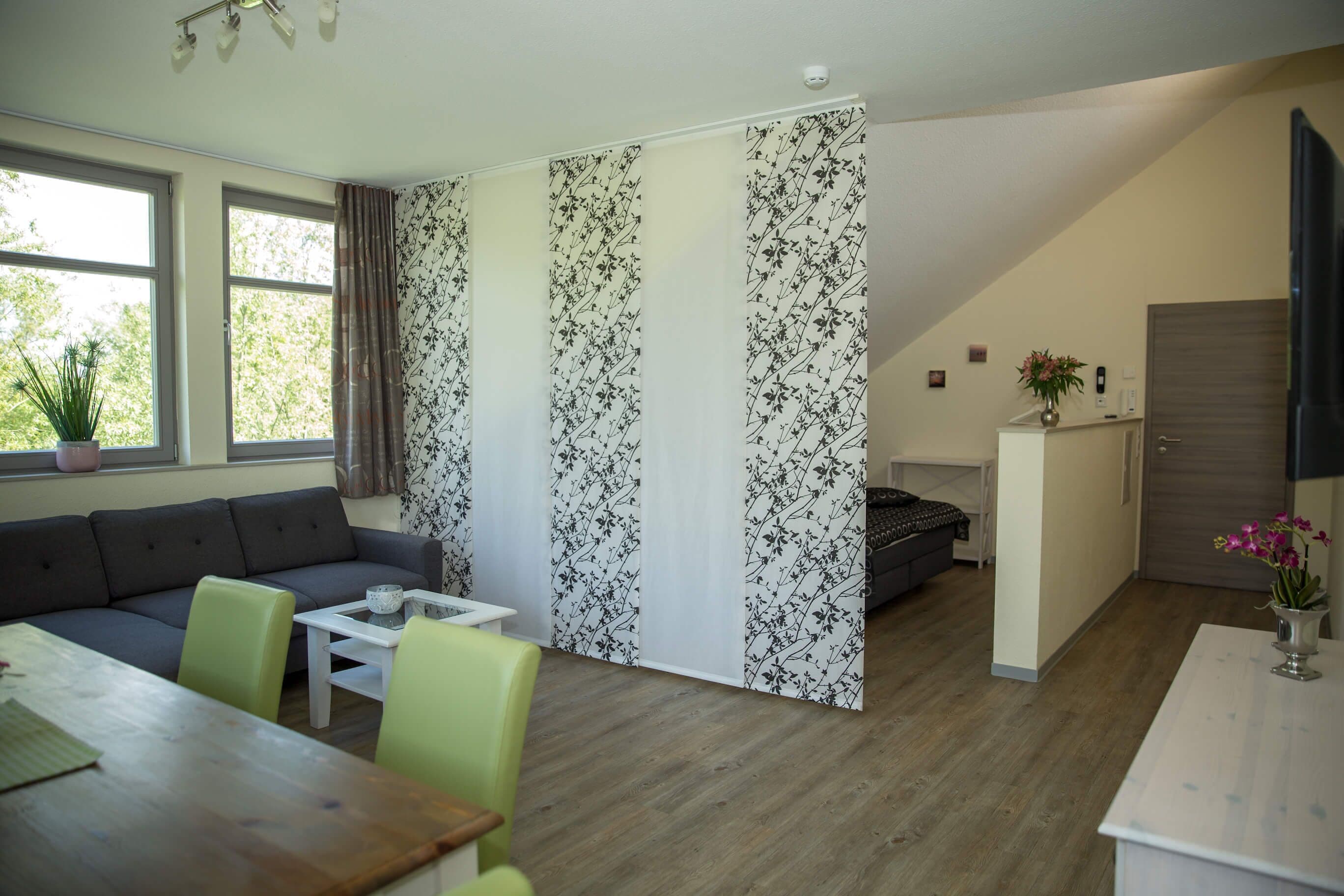 Una sala moderna con sofá, mesa de comedor y sillas. Hay una puerta corrediza con estampado floral, una mesita blanca y un aparador.