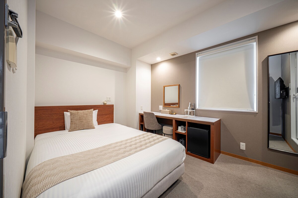 A hotel room with a large bed, a desk with a chair, a mirror, and a wardrobe.
