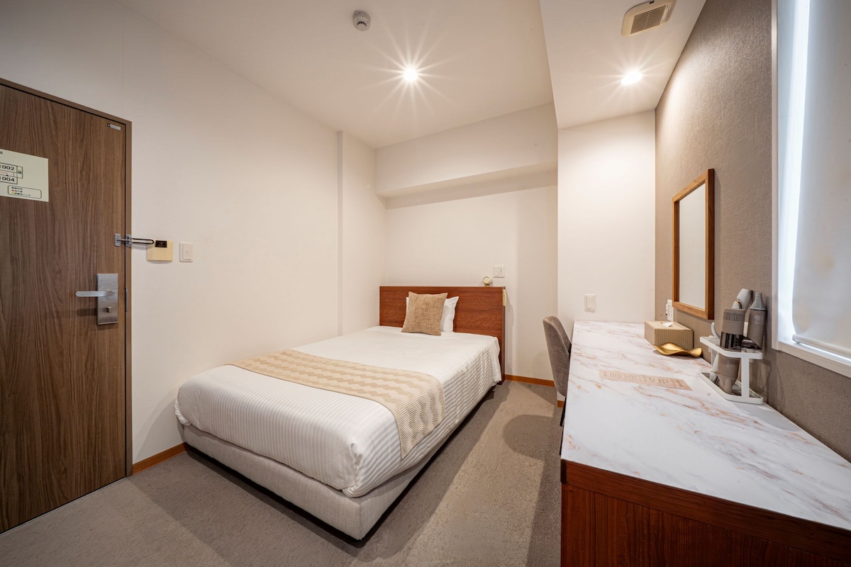 Een hotelkamer met een bed, een houten deur, een badkamer met spiegel en een wastafel met toiletartikelen.