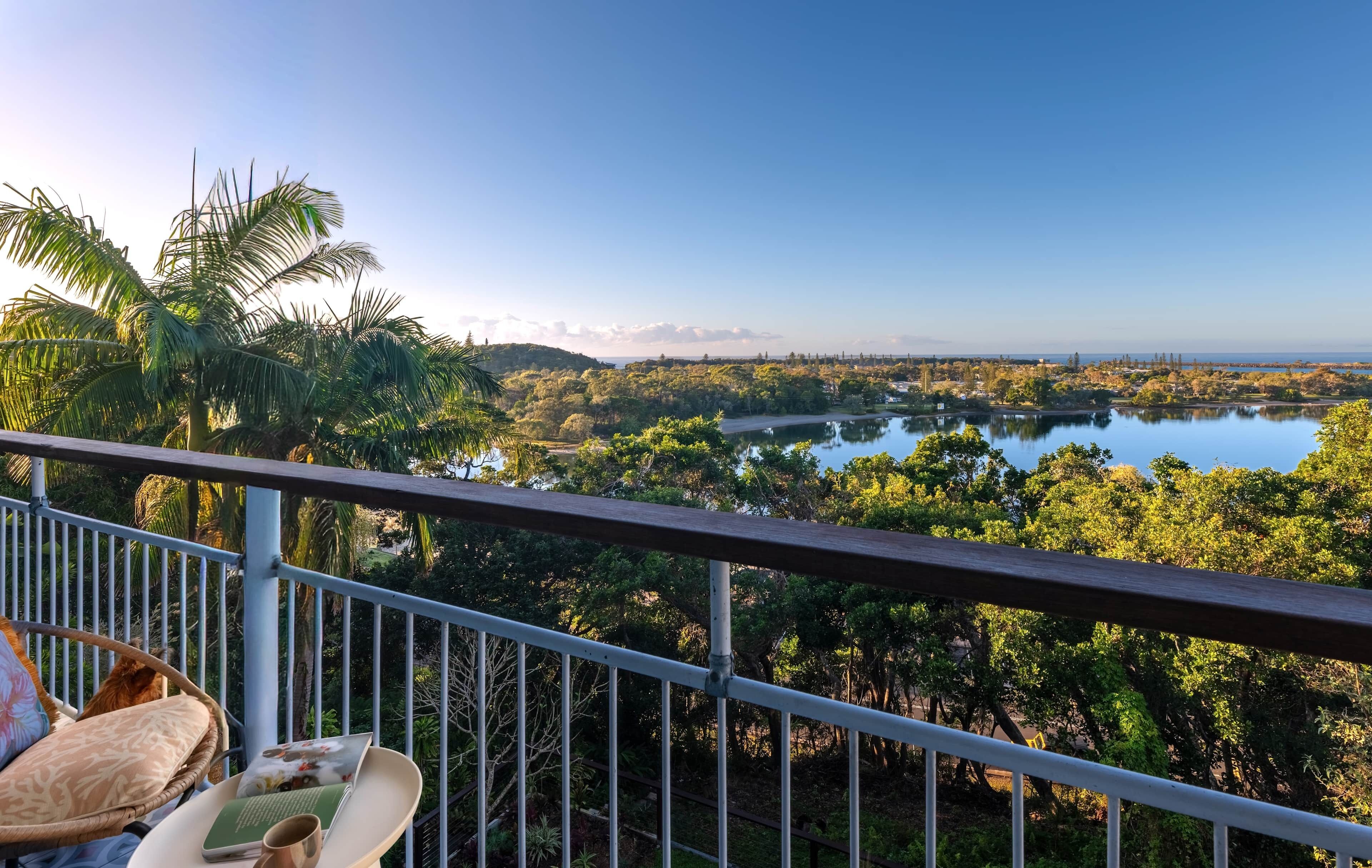 A balcony with a view of a lake, surrounded by trees and palm trees.