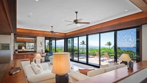 A modern living room with a large window, a sofa, a coffee table, and a lamp. - Villas at Mauna Kea 14 Two Bedroom (Kamuela)
