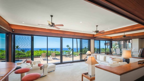 A spacious living area with a large sliding glass door leading to a balcony with a view of the ocean. There are multiple seating areas, including a sofa and two chairs, and a small bar area with stools. - Villas at Mauna Kea 14 Two Bedroom (Kamuela)