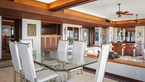 A spacious dining area with a glass table and white chairs, wooden beams on the ceiling, and ceiling fans. - Villas at Mauna Kea 14 Two Bedroom (Kamuela)