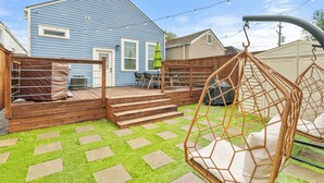 A backyard with a wooden deck, a swing chair, and a patio area with a table and chairs. - Insta Ready Meets Modern Comfort - Stylish 2BD/2BA (New Orleans)