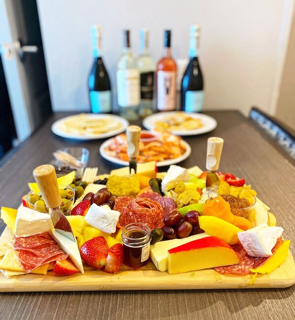 A charcuterie board with various cheeses, meats, fruits, and olives, accompanied by wine bottles in the background.