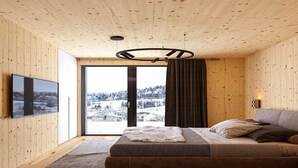 A modern bedroom with a large window, wooden walls, a sofa, and a television.