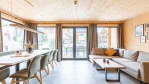 A modern living room with a wooden ceiling, a sofa, a coffee table, and a dining area with chairs and a table.