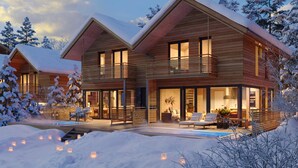 Ein modernes Holzhaus mit Pool und Sitzbereich im Freien, umgeben von schneebedeckten Bäumen.