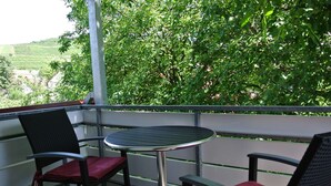 Ein Balkon mit Tisch und zwei Stühlen mit Blick auf eine üppige, grüne Landschaft.