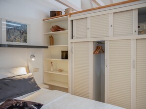 A bedroom with a bed, a bedside table, a nightstand, a wardrobe with shelves, and a hanging closet.