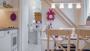 Eine moderne Küche mit weißen Schränken, ein Essbereich mit rundem Tisch und Stühlen, und ein durchgehender Blick ins Badezimmer.