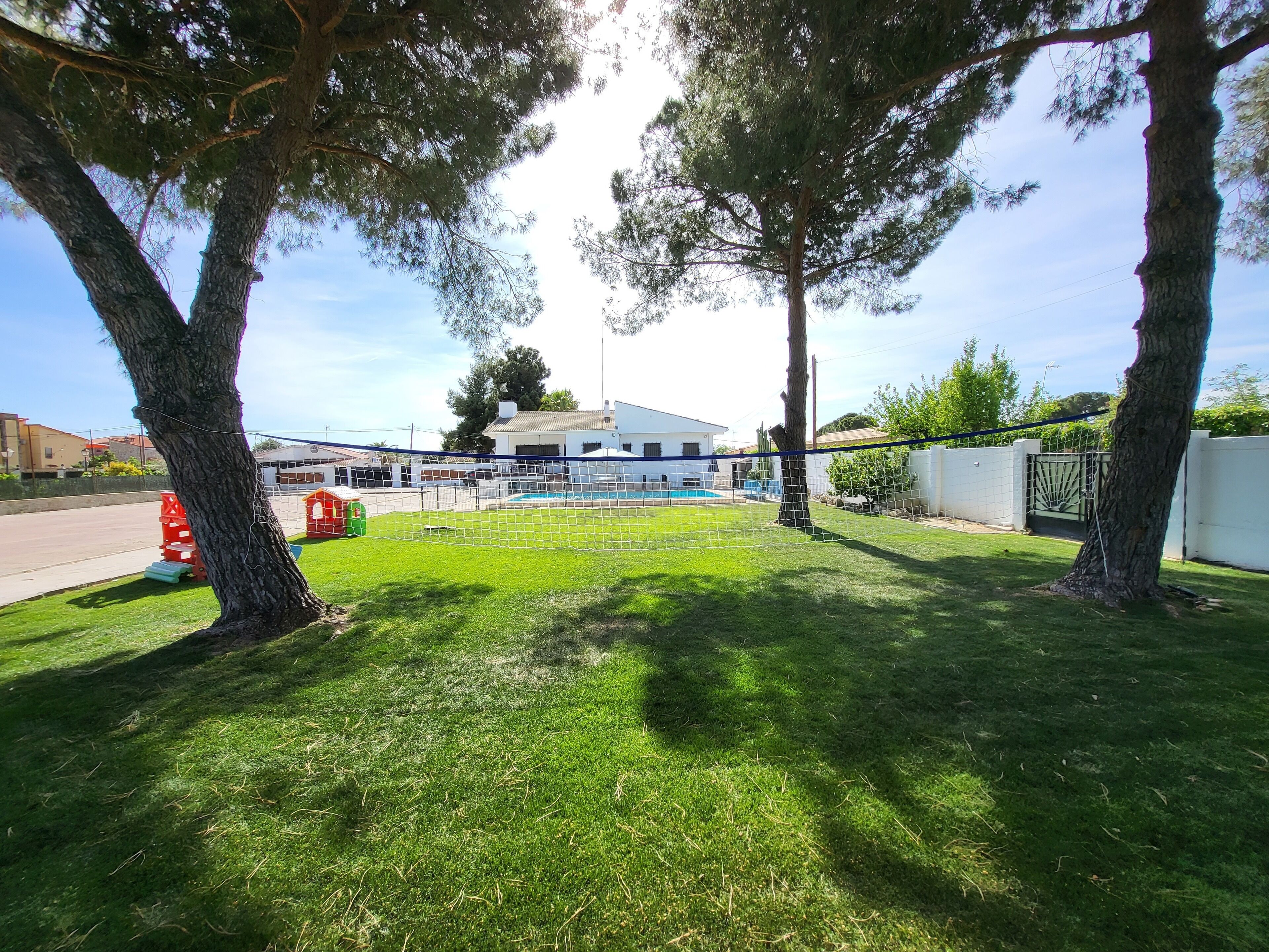 Un espacio al aire libre cercado con piscina, árboles y un edificio al fondo.
