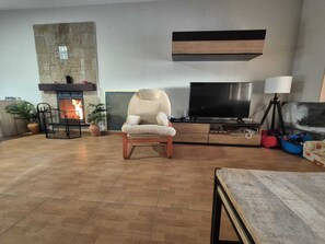 A living room with a stone fireplace, a beige armchair, a flat-screen TV, and a tripod lamp.
