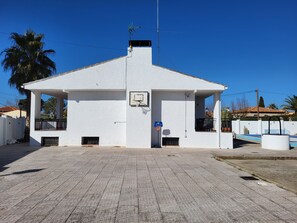 A white building with a basketball court, a covered seating area, and a palm tree in the background. - El Jardín de los Niños 2 Country House (El Viso de San Juan)