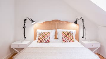 A neatly arranged bedroom with a rattan headboard, two bedside tables with lamps, and patterned pillows.