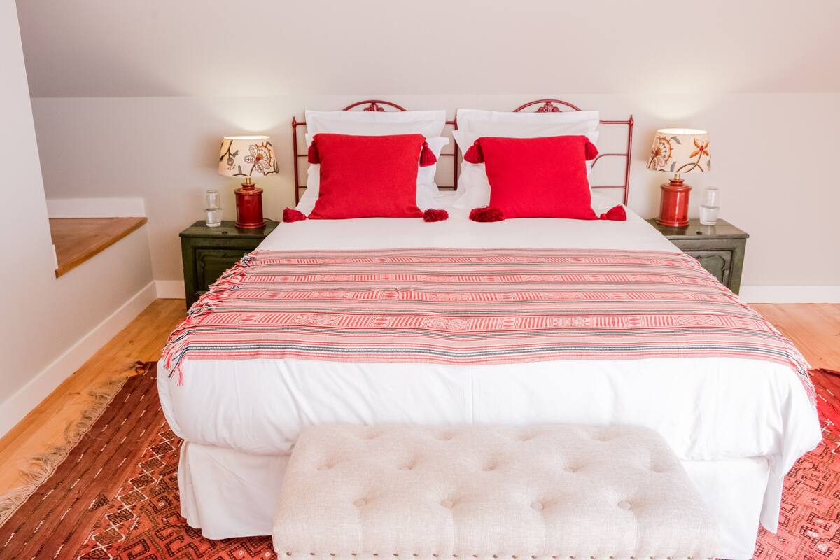 Un lit bien fait, recouvert d’une couvre-lit à motifs, avec deux oreillers rouges et un banc assorti.