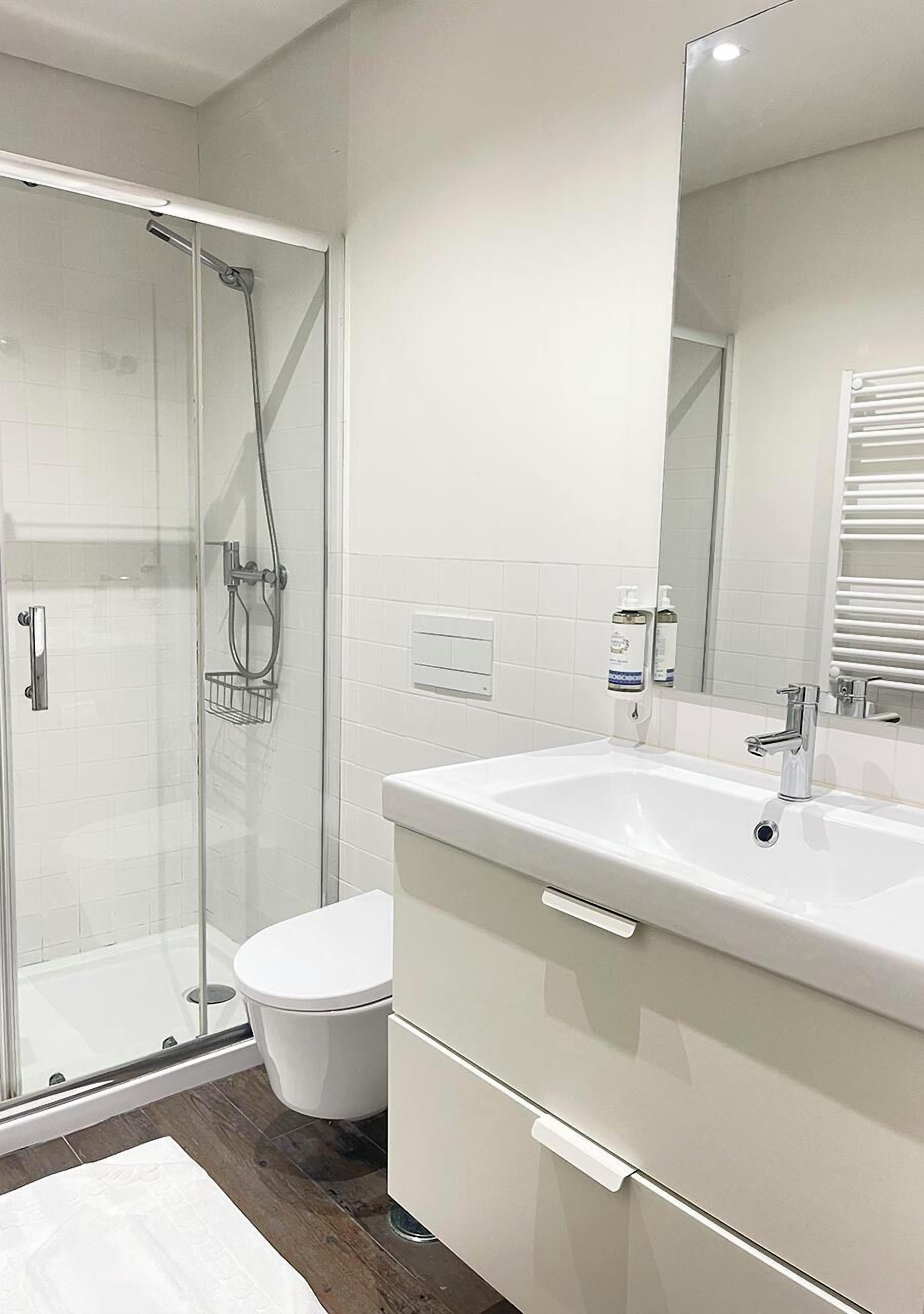 A modern bathroom with a glass-enclosed shower, a white toilet, and a vanity with a mirror.
