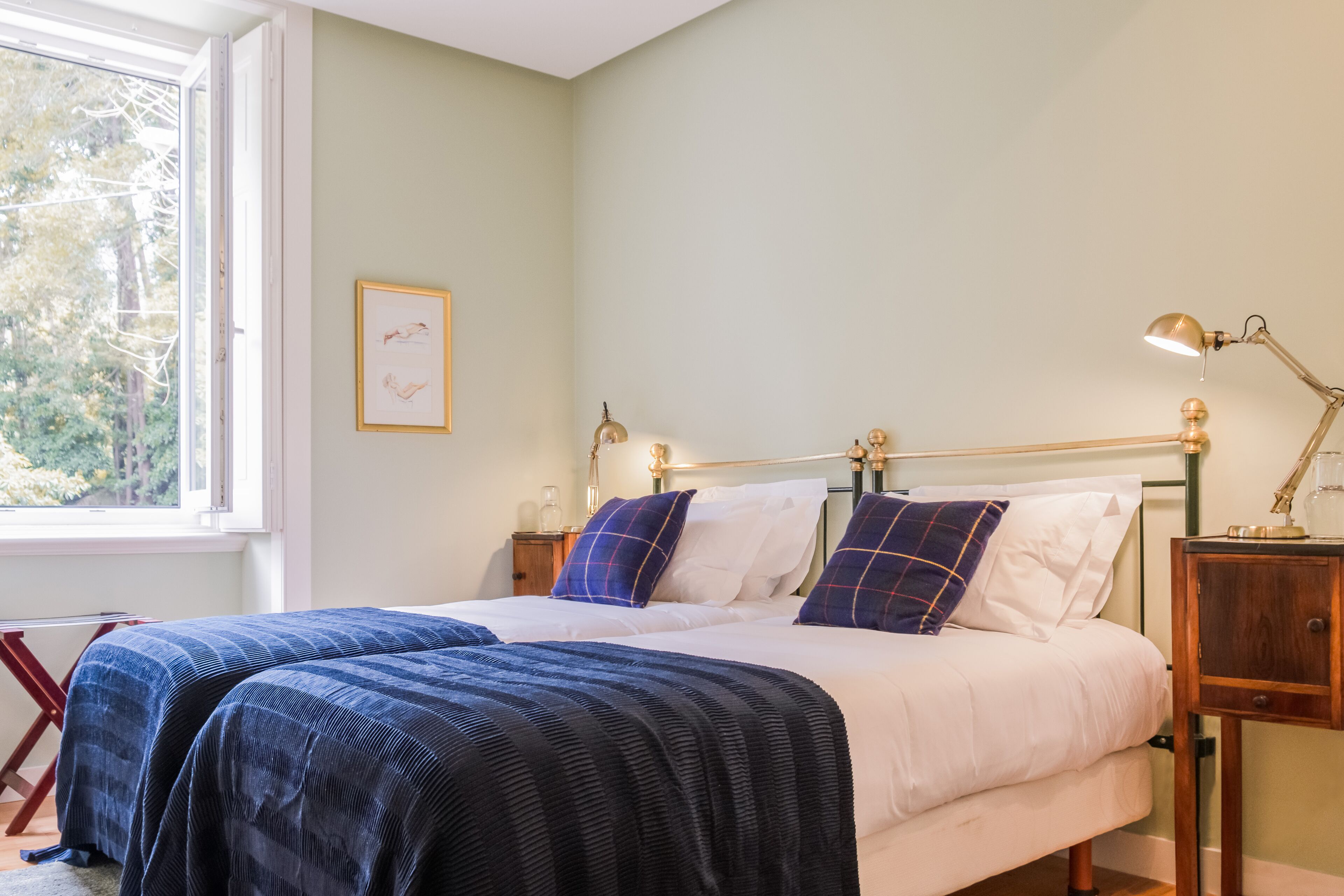 A bedroom with two beds, a window, and a bedside table with a lamp.