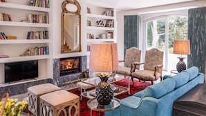 Een woonkamer met een open haard, boekenkasten, een blauwe bank en twee fauteuils.