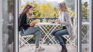 Twee personen zitten aan een tafel met uitzicht op bomen en bergen.