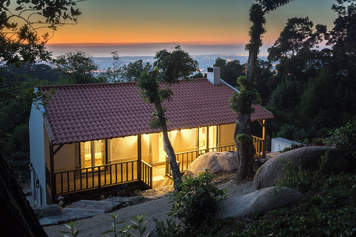 A house with a red-tiled roof, a balcony, and a view of the city at sunset.