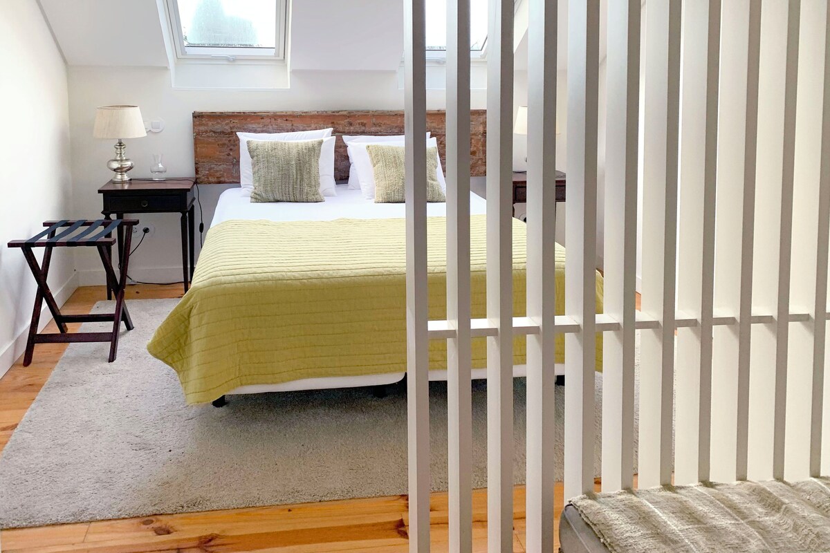 Une chambre à coucher avec un lit, une table de chevet, une lampe, une fenêtre et une vue sur le ciel.