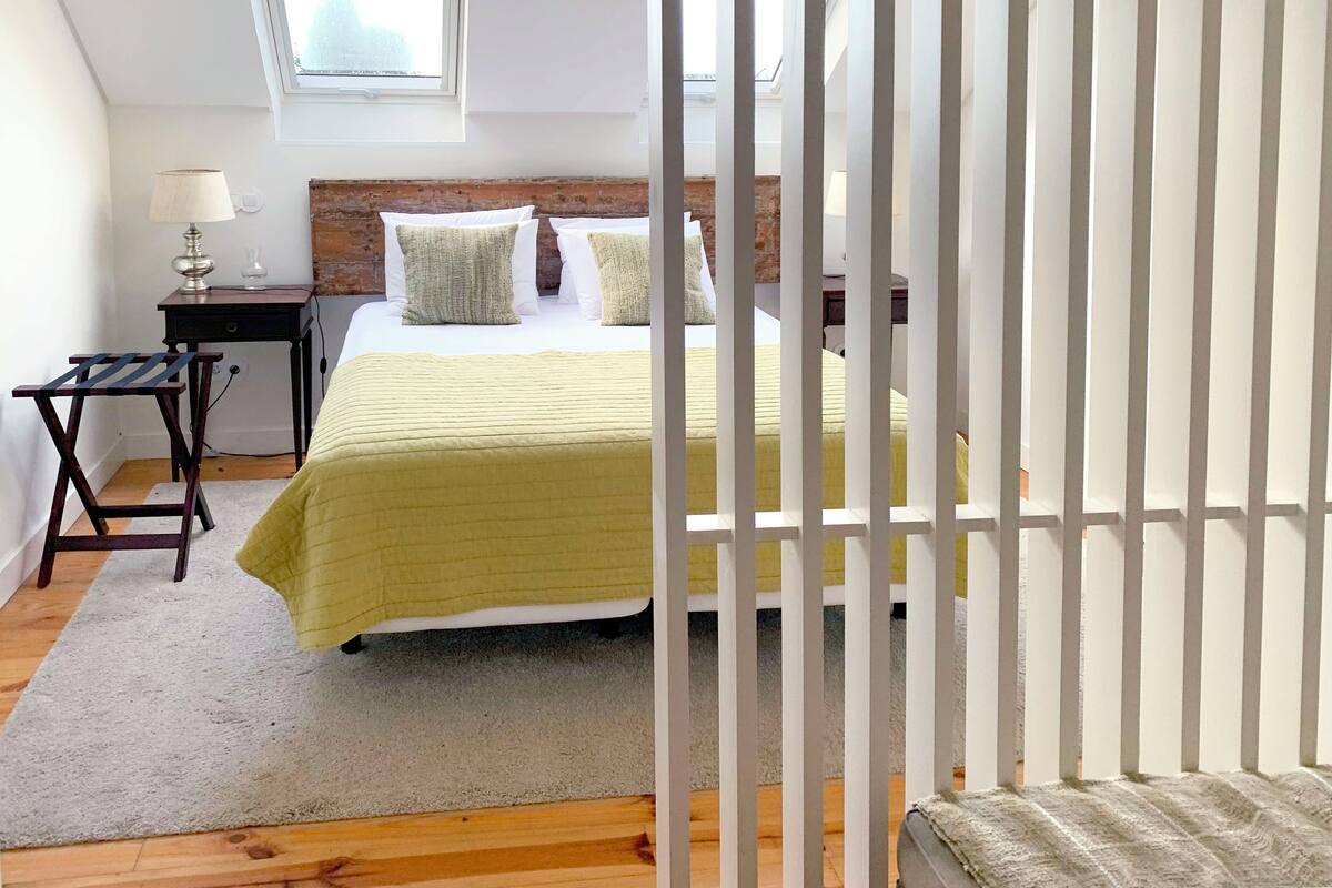 Une chambre à coucher avec un lit, une table de chevet, une lampe, une fenêtre et une vue sur le ciel.