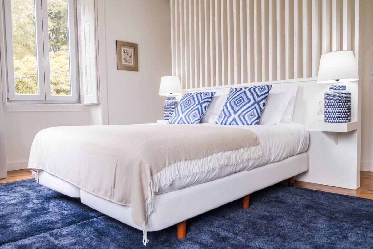 Une chambre à coucher comprenant un lit, une fenêtre, une table de chevet avec une lampe et une étagère fixée au mur.