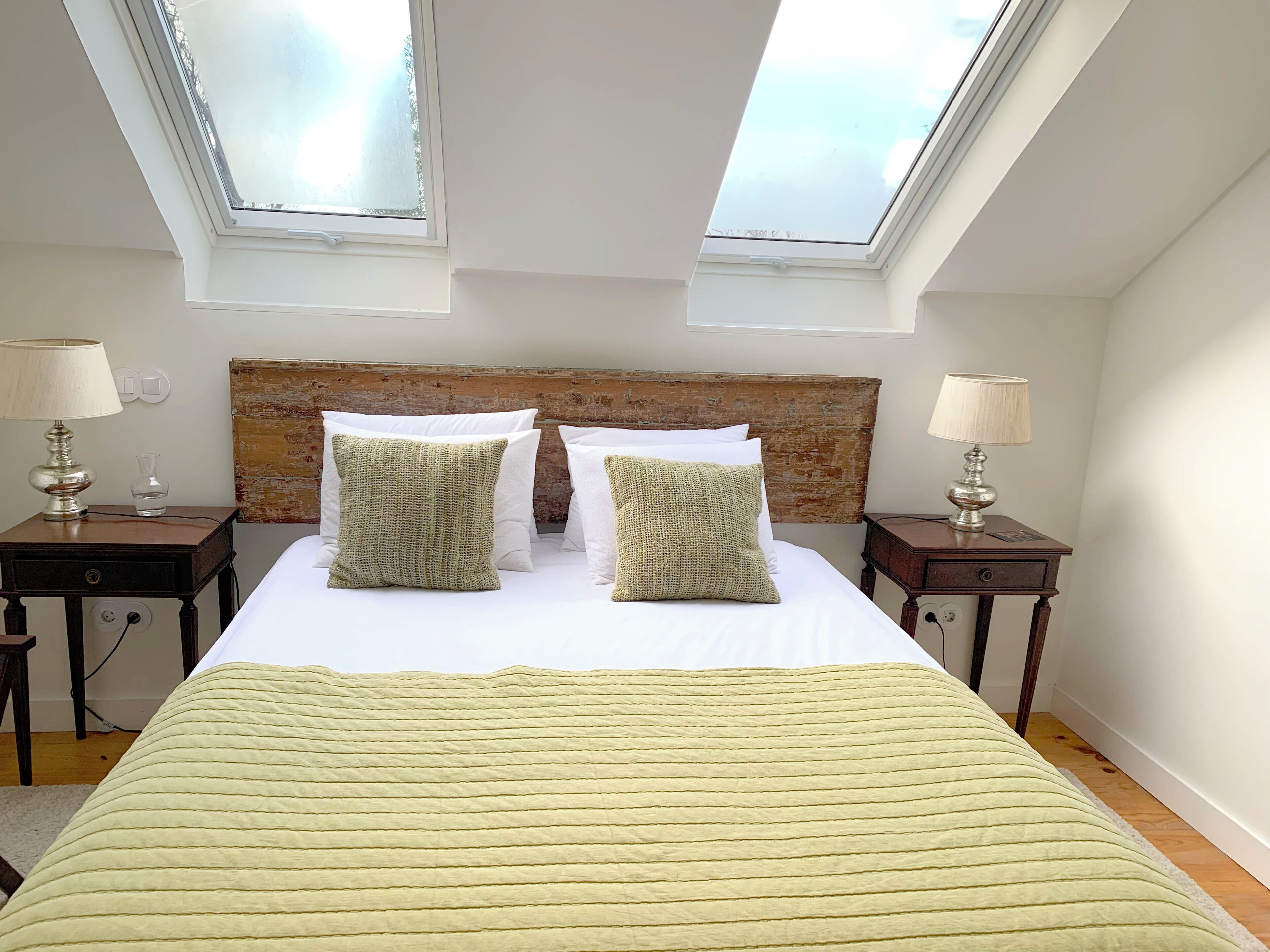 A bedroom with a bed, two nightstands, two lamps, a wooden headboard, and skylights.