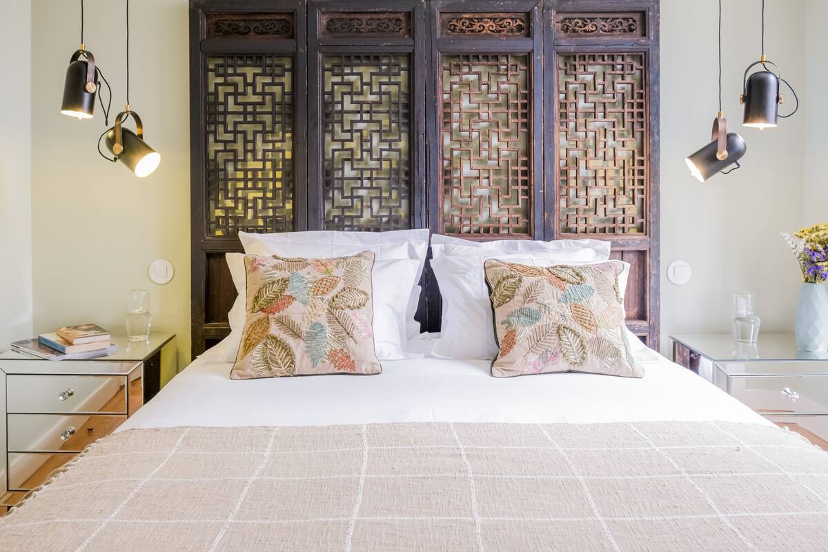 Une chambre à coucher bien aménagée, avec un grand lit, deux tables de chevet et un paravent décoratif en bois placé derrière le lit.