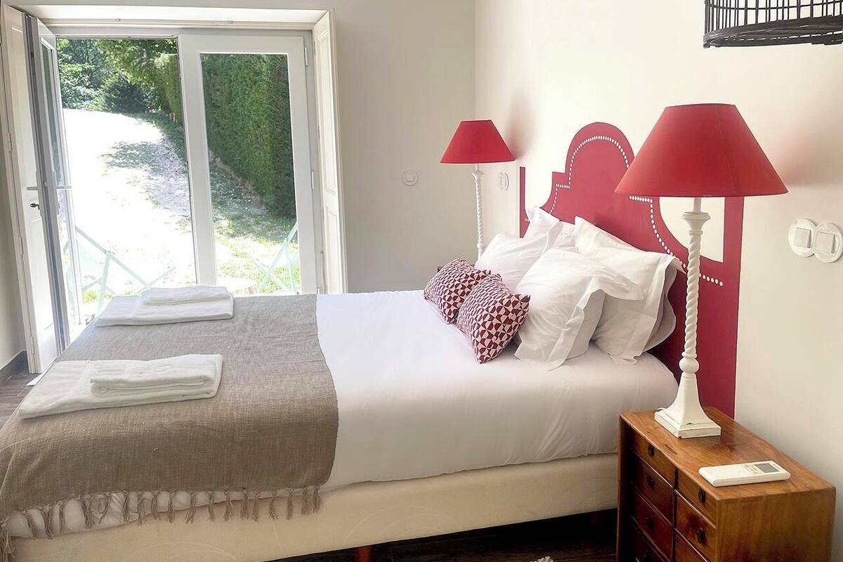 Une chambre à coucher avec un lit, deux lampes de chevet, une table de chevet et une fenêtre donnant sur un paysage verdoyant.